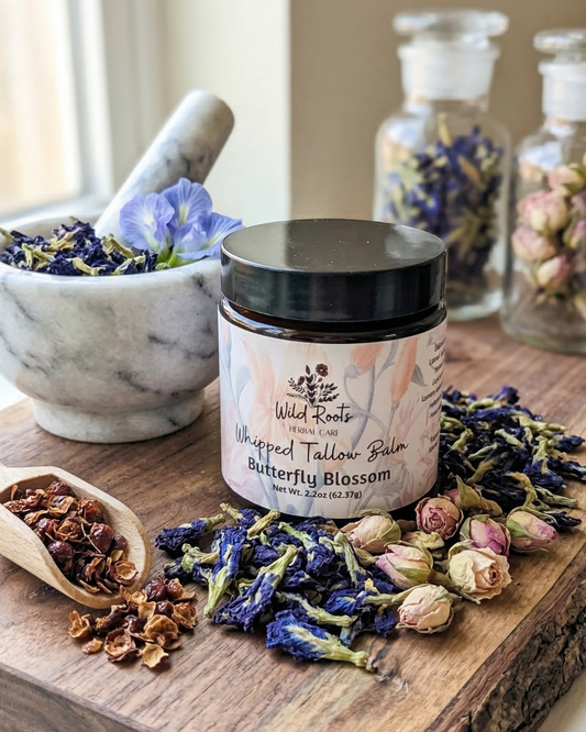 Whipped tallow balm jar labeled 'Butterfly Blossom' on a wooden surface with dried flowers and herbs.