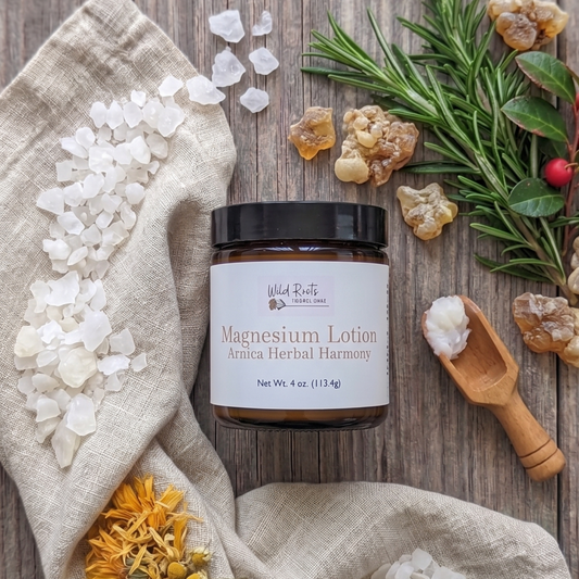 A jar of Wild Bells Magnesium Lotion sits on a rustic wooden surface, styled with a beige linen cloth, crystals, rosemary, amber pieces, dried flowers, and a small wooden spoon with white lotion.