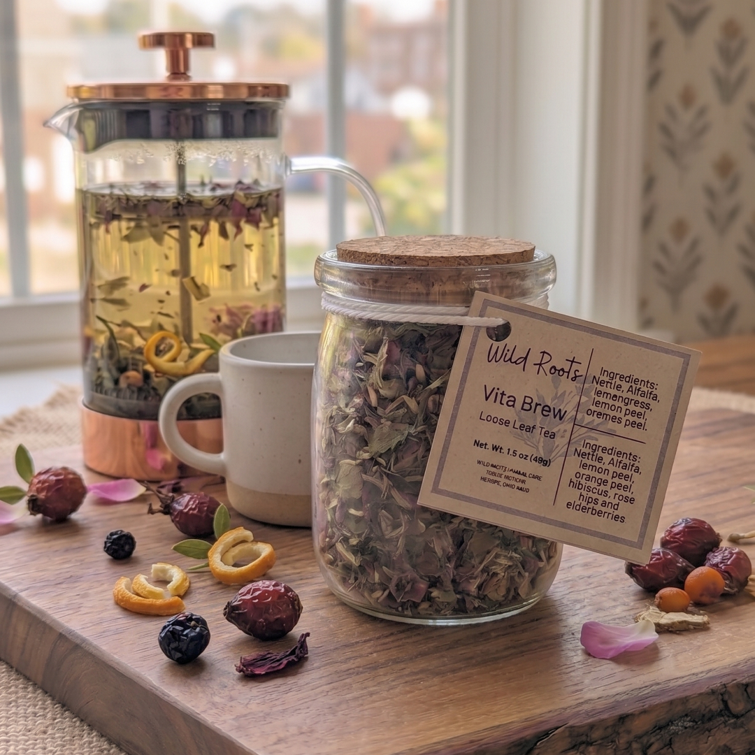 Jar of dried herbs with a tag, mug, and tea press on a wooden surface.