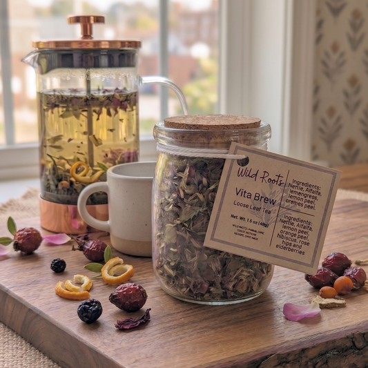 Jar of dried herbs with a tag, mug, and tea press on a wooden surface.