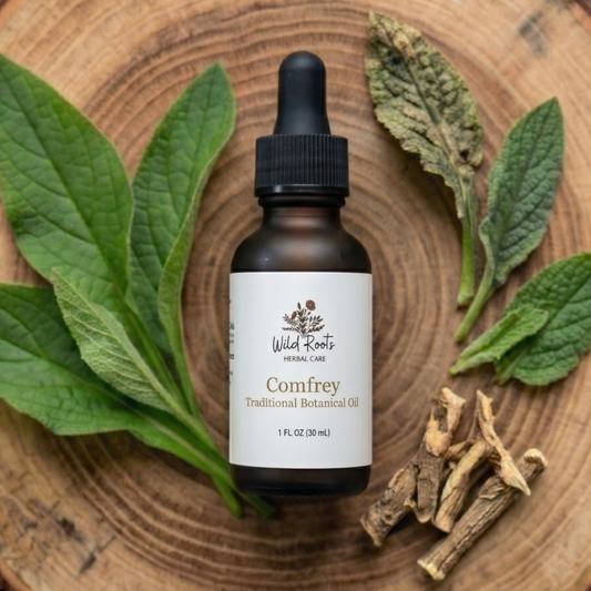 Bottle of Wild Roots Herbal Care Comfrey Traditional Botanical Oil on a wooden surface with comfrey leaves and roots.