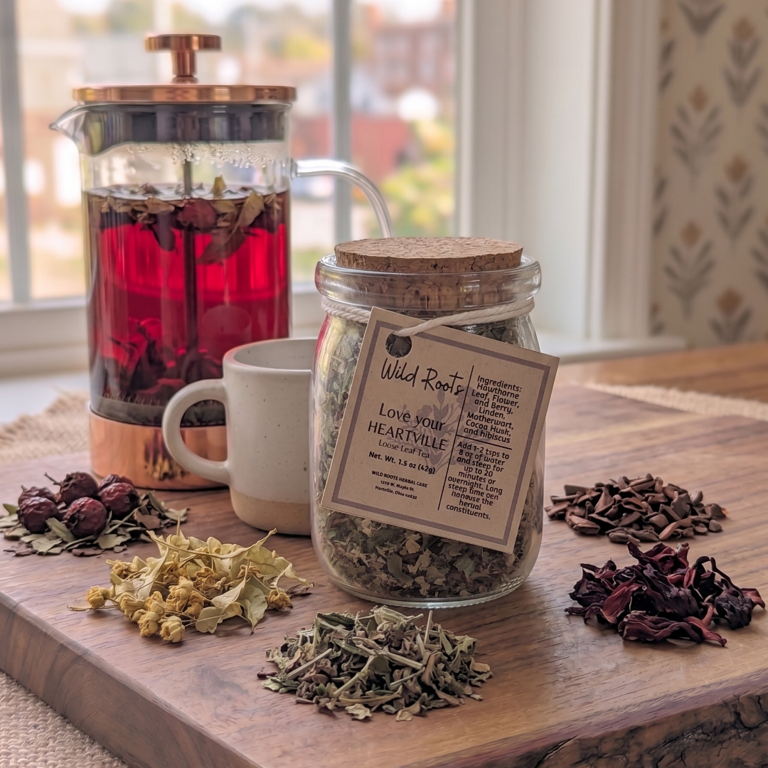 Tea-making setup with a jar of dried herbs, a teapot with red liquid, and a mug on a wooden surface.